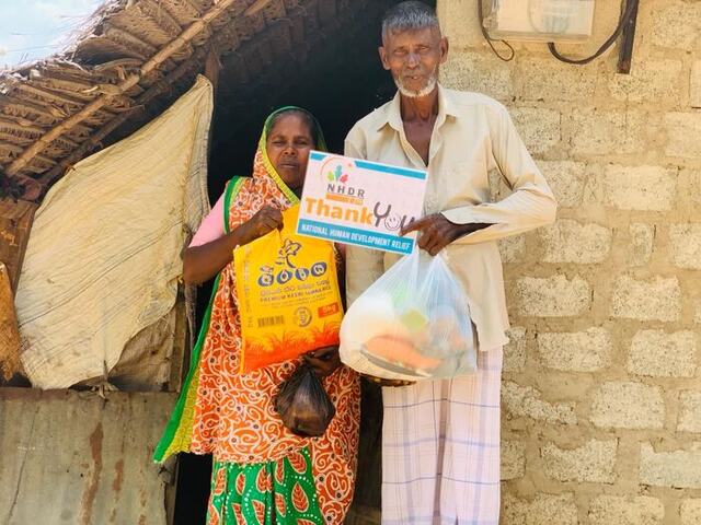 An elderly couple receiving a rice bag and grocery parcel from NHDR