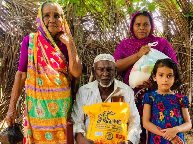 An elderly couple and their granddaughter with NHDR relief supplies